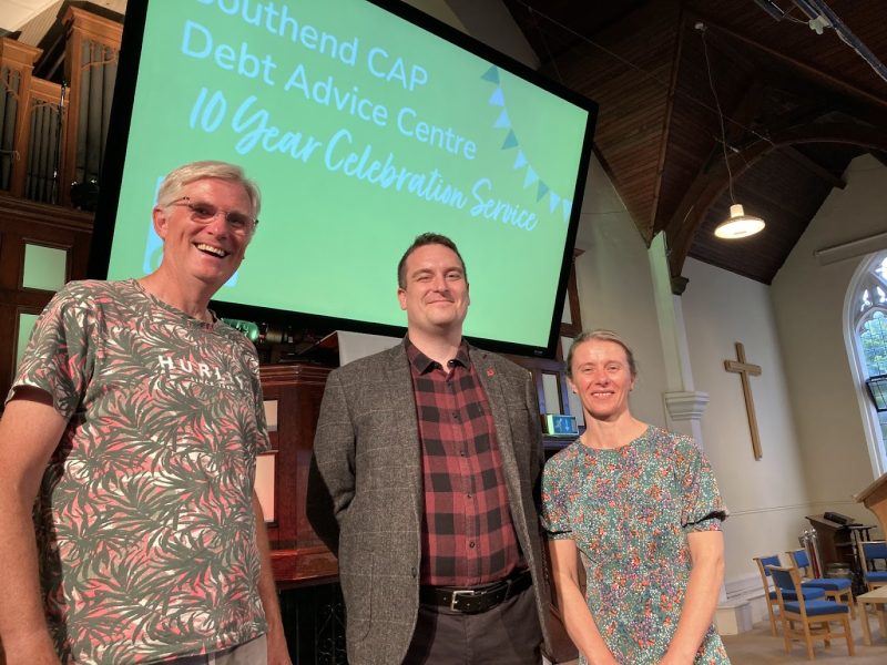 three members of the Southend CAP Debt Advice Centre stand in front of screen with their logo on it